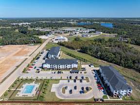 A bird's eye view of a parking lot with a swimming pool and a building in the background.