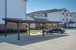 A motorcycle is parked under a canopy next to a car in a parking lot.