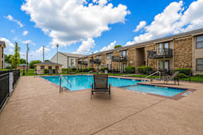 A swimming pool in a residential area with a chair and a poolside table.