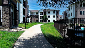 A long concrete walkway leads through a grassy area between two rows of apartment buildings.