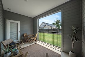 Flat Creek Apartments patio with a table and chairs overlooks a green lawn and a house.
