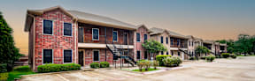 A row of red brick apartment buildings with green bushes in front.