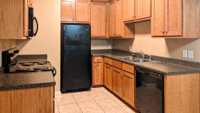 a kitchen with wood cabinets and black appliances at the Corners Apartments