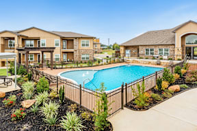 A swimming pool surrounded by a black fence and landscaping.
