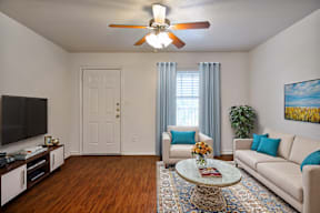 A living room with a white couch, a coffee table, a ceiling fan, and a painting on the wall.