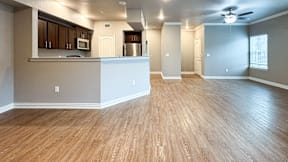 A spacious living room with hardwood floors and a kitchen area in the background.