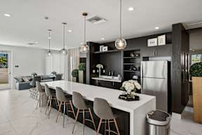 A modern kitchen with a long white island and grey chairs.
