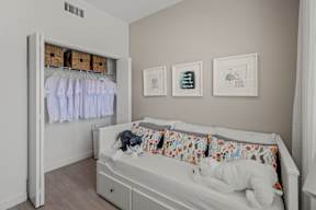 A white bed with a stuffed animal on it in a room with a white wardrobe.