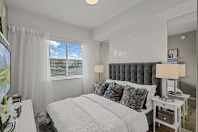A bedroom with a large bed, a nightstand with a lamp, and a TV on the wall.