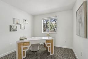 A white desk with a chair and a table with a lamp on it.