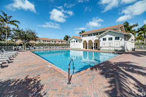 A large swimming pool surrounded by a brick patio and a white building in the background.