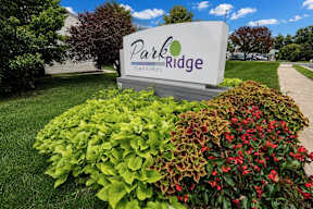 A sign for Park Ridge Townhomes is surrounded by green and red bushes.