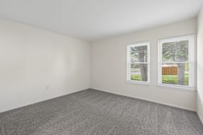A room with a grey carpet and two windows.