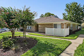 A house with a white fence and a tree with pink flowers in front.