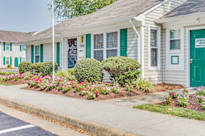 a white house with green shutters and a flower garden in front of it