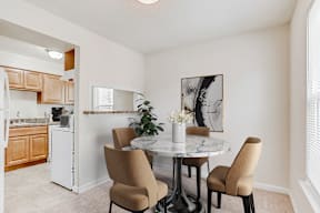 a dining area with a table and chairs and a kitchen in the background