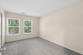 A room with a grey carpet and two windows.