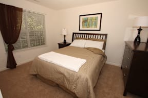 Bedroom with queen size bed, nightstand, dresser and large window.
