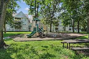 A playground with a green slide and picnic table in front of apartment buildings.