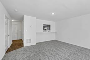 A spacious, empty room with a grey carpet and white walls.