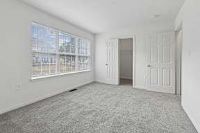 A room with a carpeted floor, a large window with blinds, and a door leading to another room.