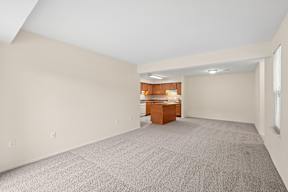 A large empty room with a carpeted floor and a wooden cabinet in the corner.