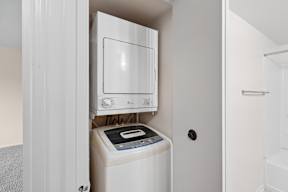 A white microwave oven is built into a cabinet above a washing machine.