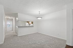 A spacious living room with a carpeted floor and a bar area in the background.