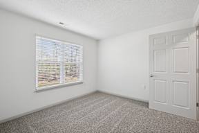A room with a white door, carpeted floor, and a window with blinds.