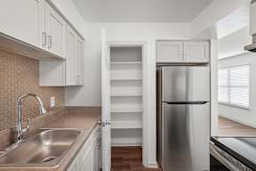 A kitchen with a stainless steel refrigerator and a sink with a brick backsplash.