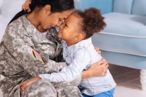 a woman in a military uniform is sitting on the floor and smiling at a little girl