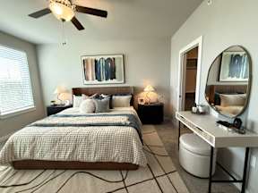 A bedroom with a large bed, a vanity with a mirror, and a ceiling fan.