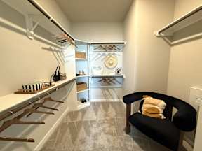 A room with a black chair and a rack of clothes.