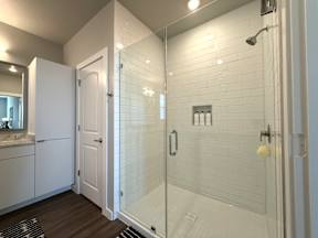 A white tiled shower with a glass door and a white cabinet.