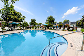A large outdoor swimming pool with a blue sky and trees in the background.