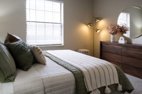 furnished apartment bedroom with a well-made bed facing a wood dresser