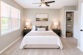A bedroom with a large bed, two lamps, and a ceiling fan.