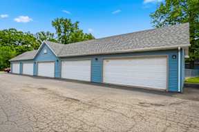 A blue garage with white doors is surrounded by a cracked parking lot.