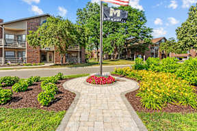 A garden with a flag pole in front of apartment buildings.