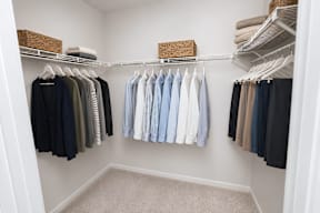 A white closet with clothes hanging on shelves and hangers.