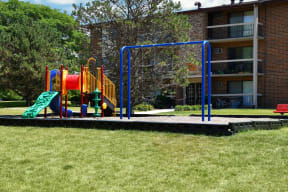 a playground in the middle of a grassy area with a brick building in the background