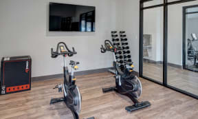 stationary bikes in front of a mounted TV in the Willow Crossing Apartments fitness center