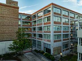 A large red brick building with many windows and a tree in front.