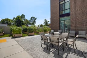a patio with a wooden table and chairs and a brick building in the background