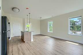 A spacious kitchen with wood flooring and a refrigerator on the left.