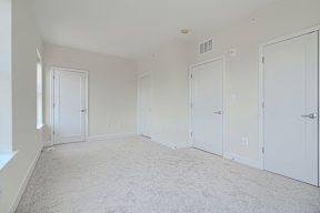 A room with white walls and carpeted floor with four doors.