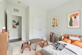 A bedroom with a bed, a chair, a table, and a painting on the wall.