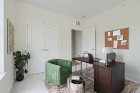 A green chair sits in a room with a desk and a bulletin board on the wall.