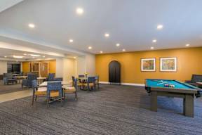 A room with a pool table and chairs.