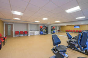 A gym with exercise equipment and a wall of windows.